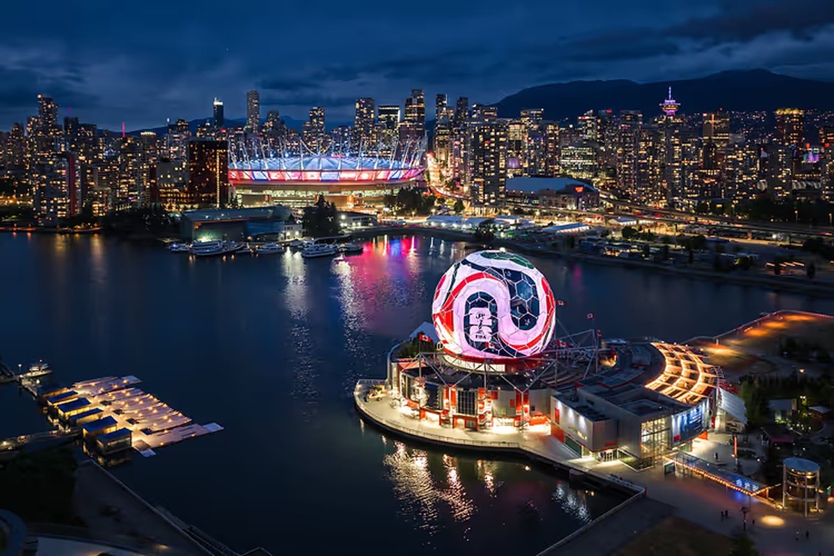 Night aerial of Vancouver's False Creek with BC Place lit up and an illuminated FIFA World Cup match-ball structure on the water