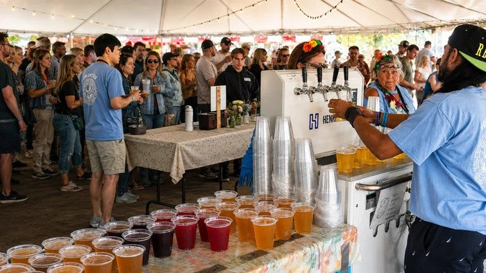 Guests at a festival tent collecting cups of different coloured beer poured from a Henrik machine